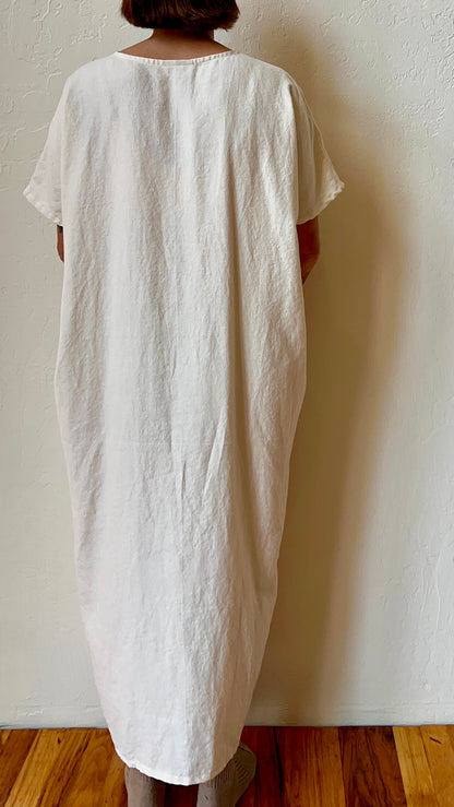 Person wearing a long white dress against a plain wall.