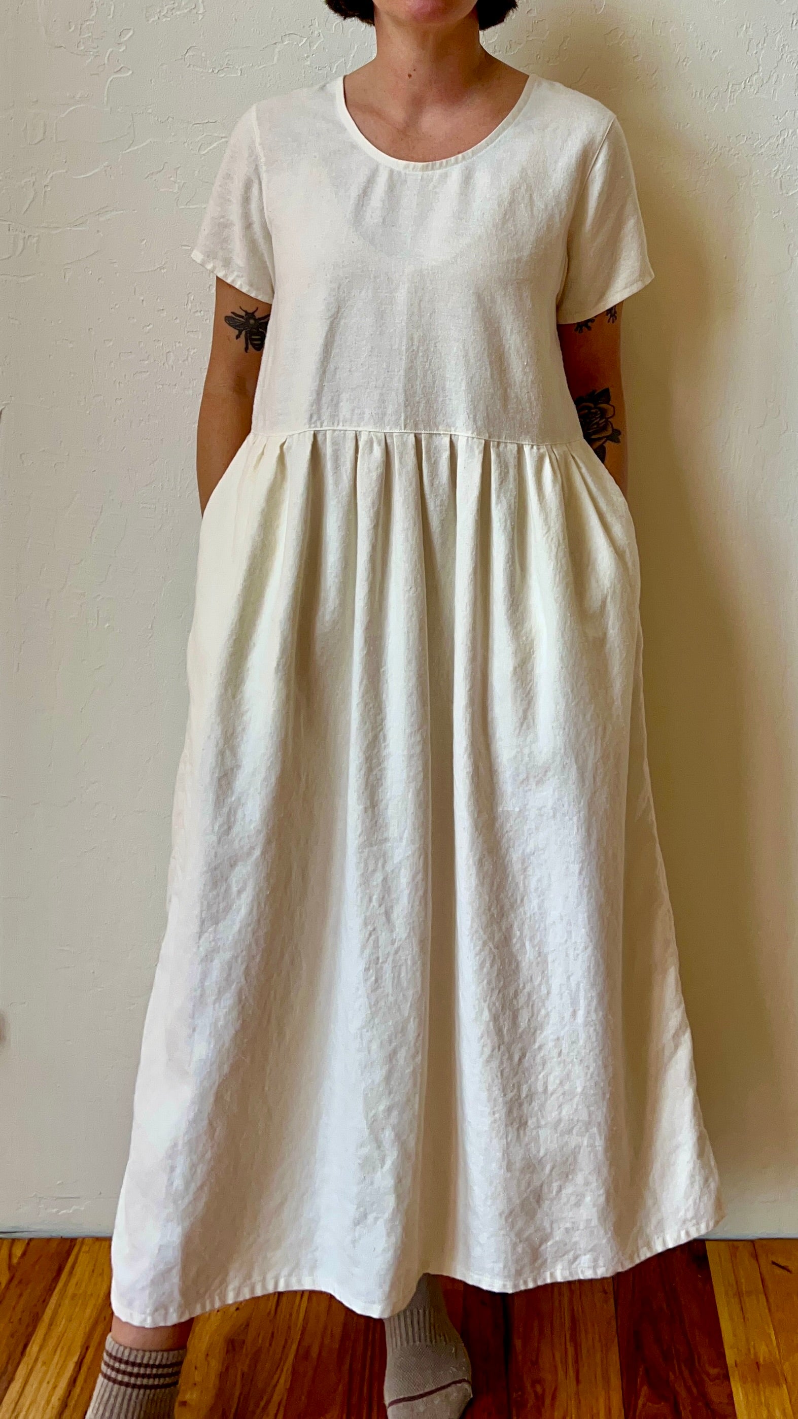 Person wearing a long white dress against a plain wall.