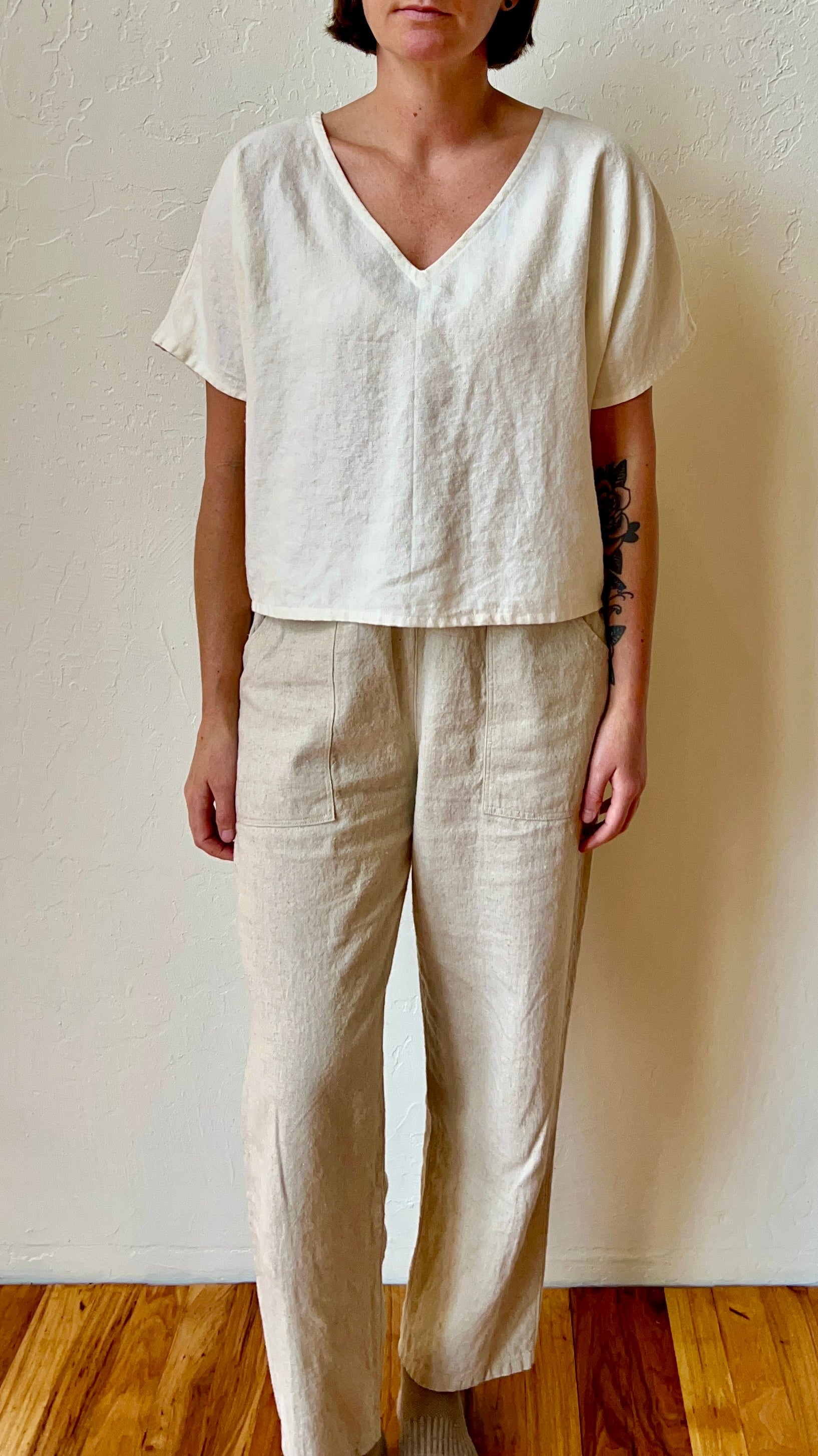 Person wearing a white top and beige pants against a plain wall.