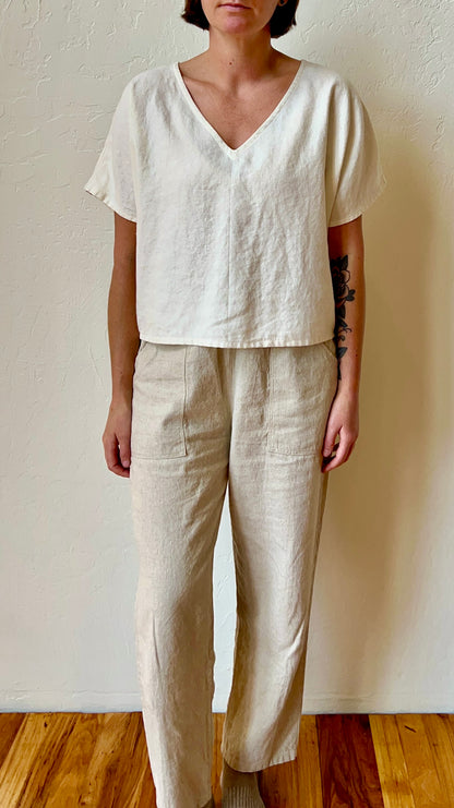 Person wearing a white top and beige pants against a plain wall.