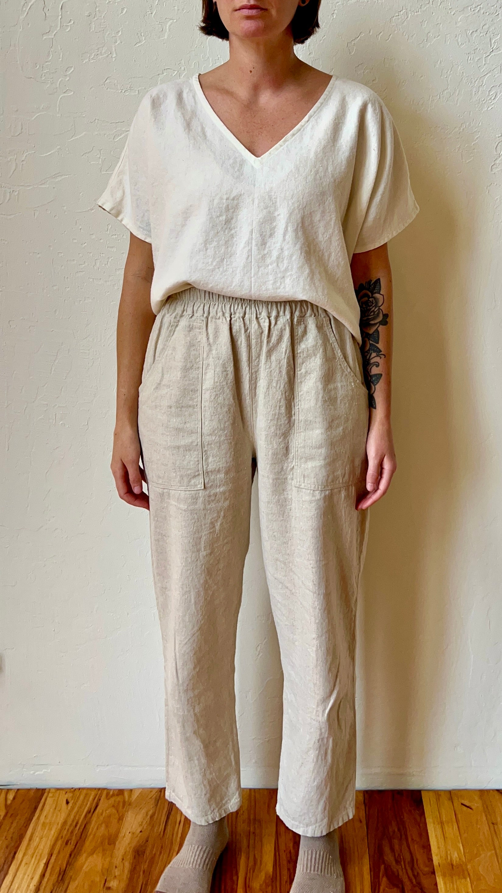 Person wearing a white hemp top and beige pants against a plain wall.