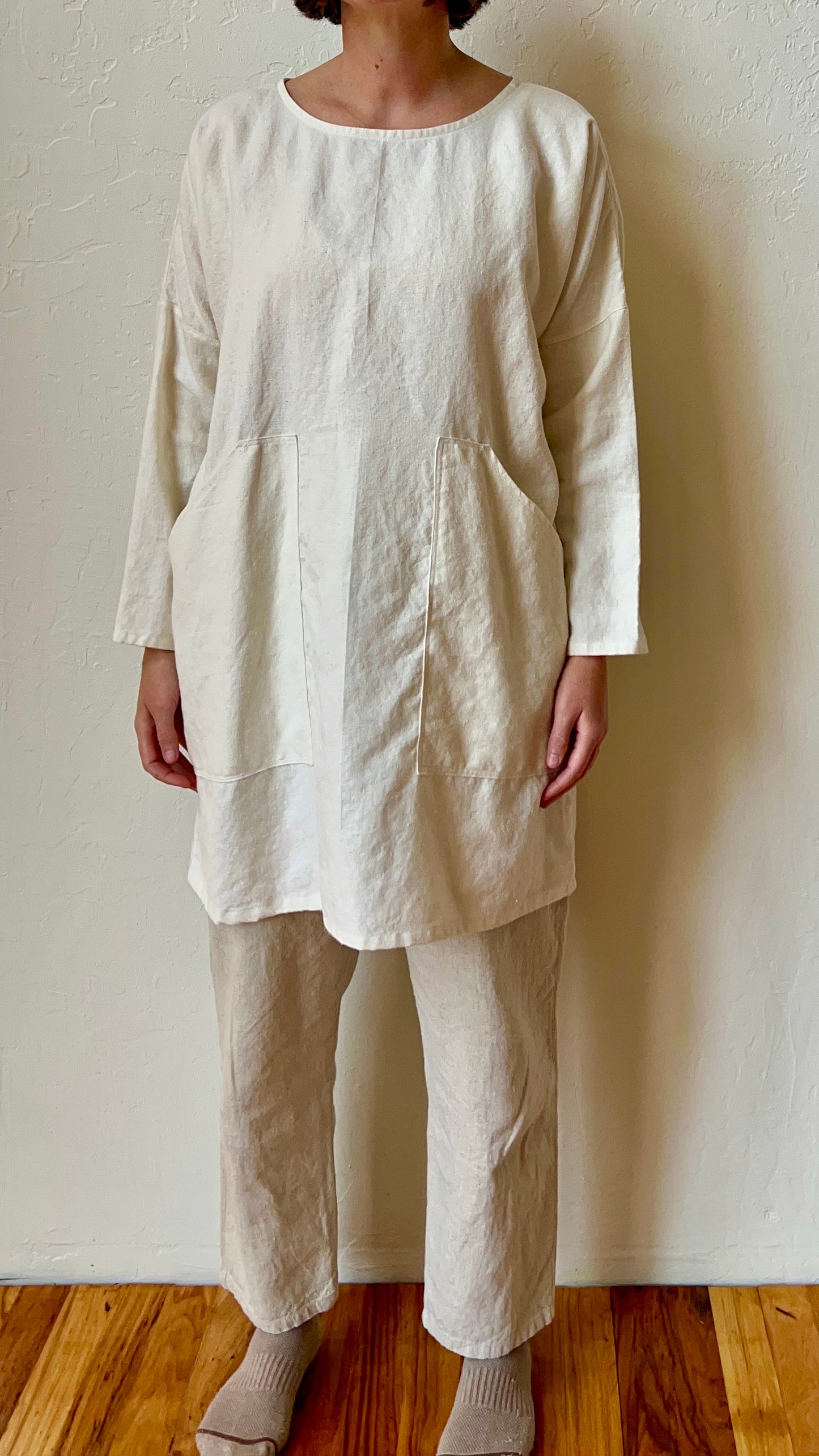 Person wearing a beige linen outfit against a plain wall.