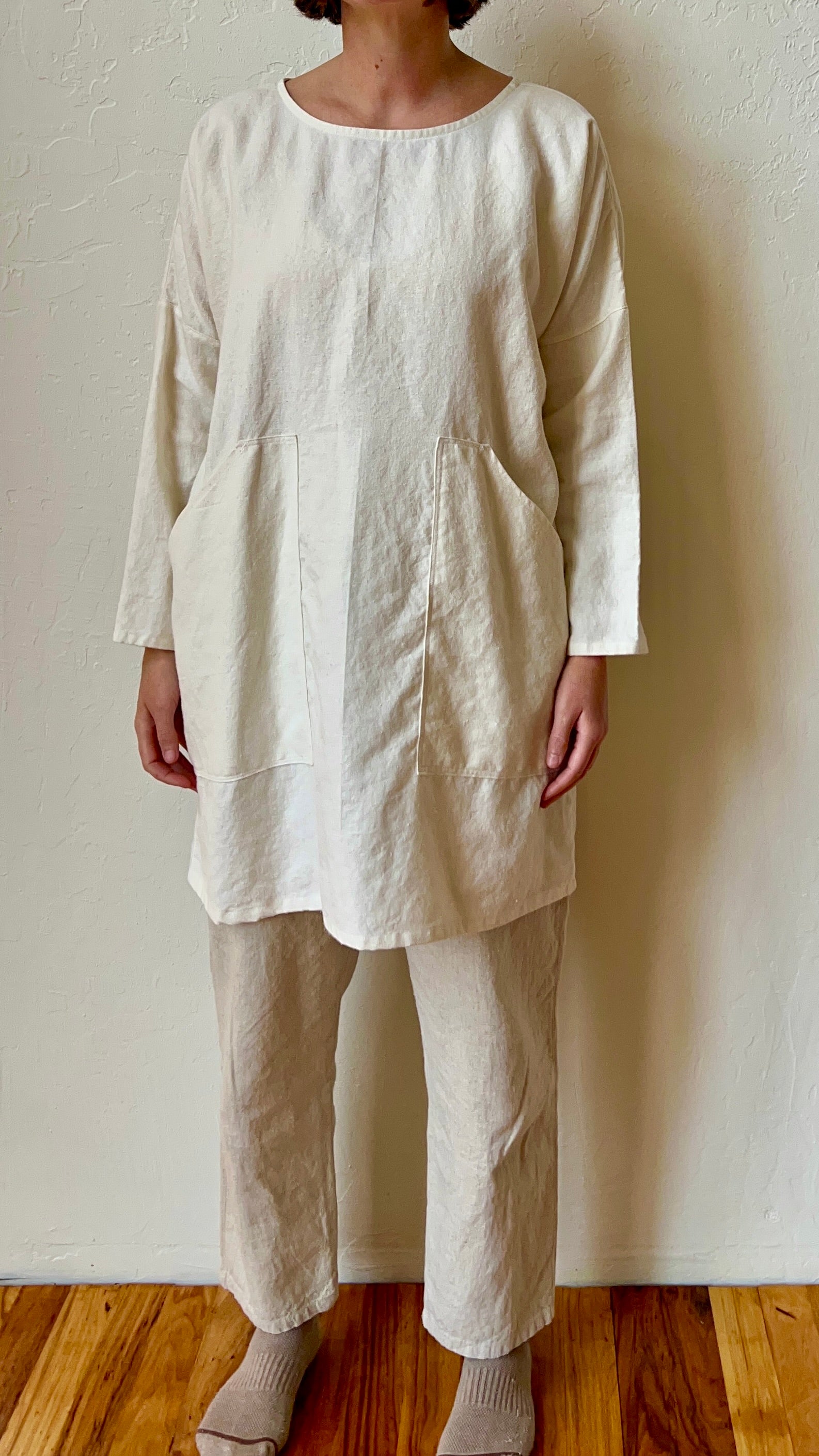 Person wearing a beige linen outfit against a plain wall.