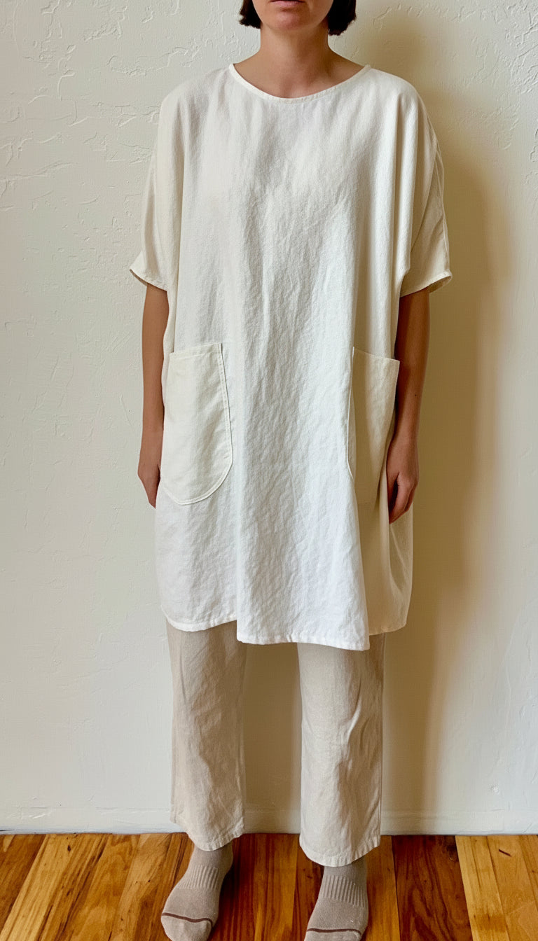 Person wearing a loose-fitting, off-white hemp dress with wide-leg pants against a plain wall.