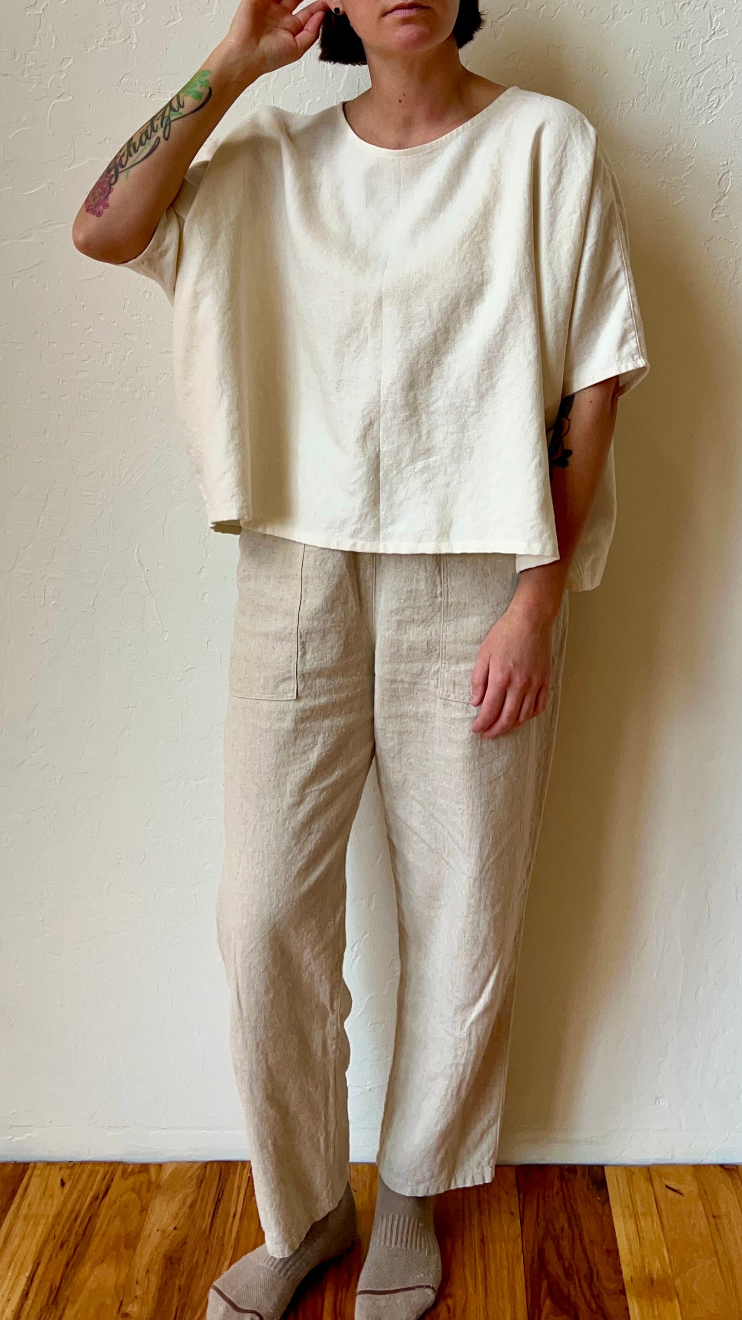 Person wearing a beige top and pants against a white wall.