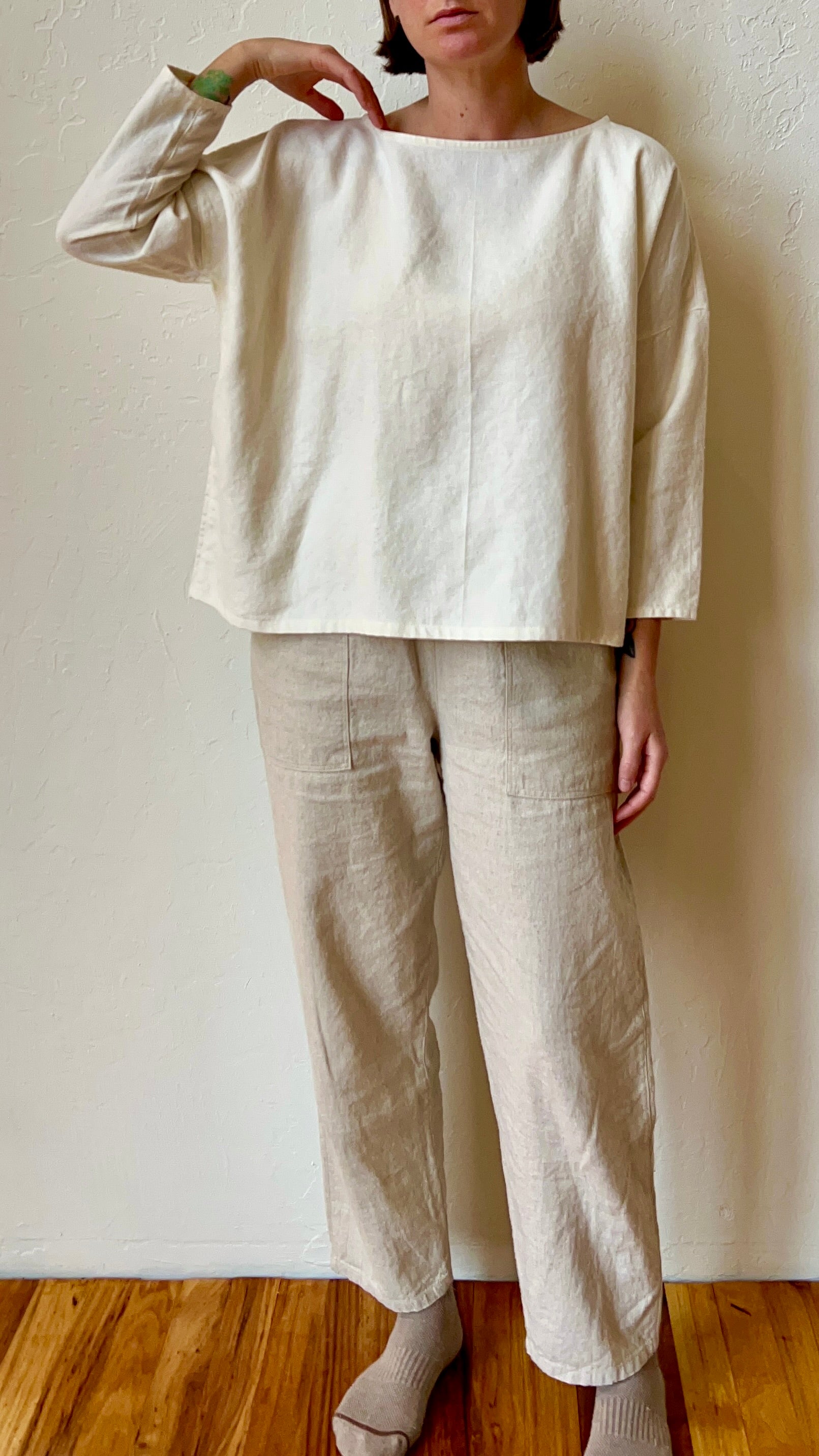 Person wearing a white top and beige pants against a plain wall.