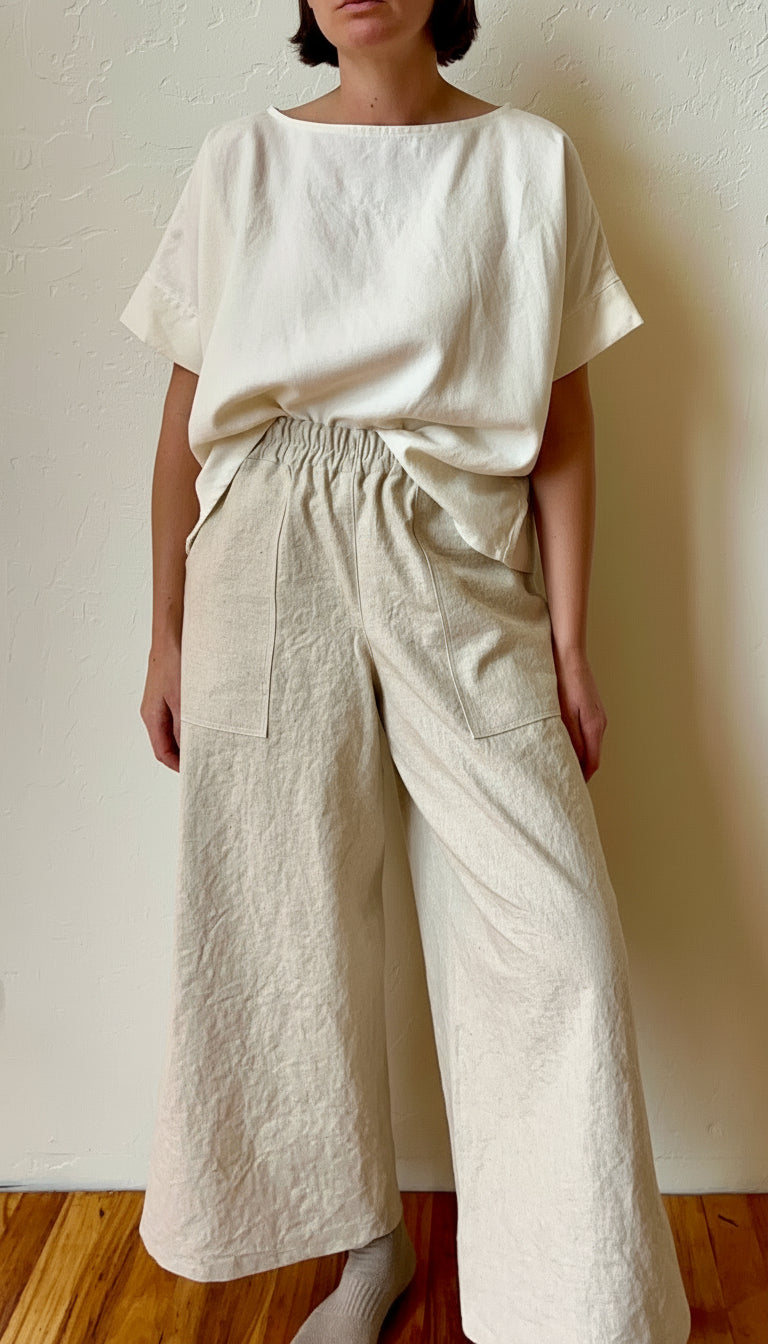 Person wearing a white hemp fabric top and beige wide-leg pants against a plain wall.