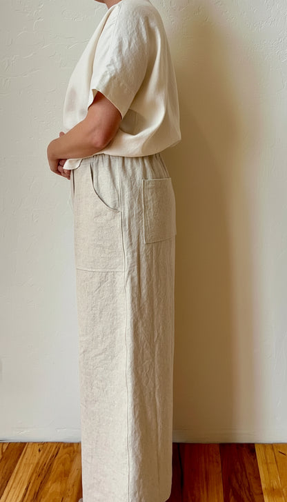 Person wearing a white shirt and beige pants against a plain wall.