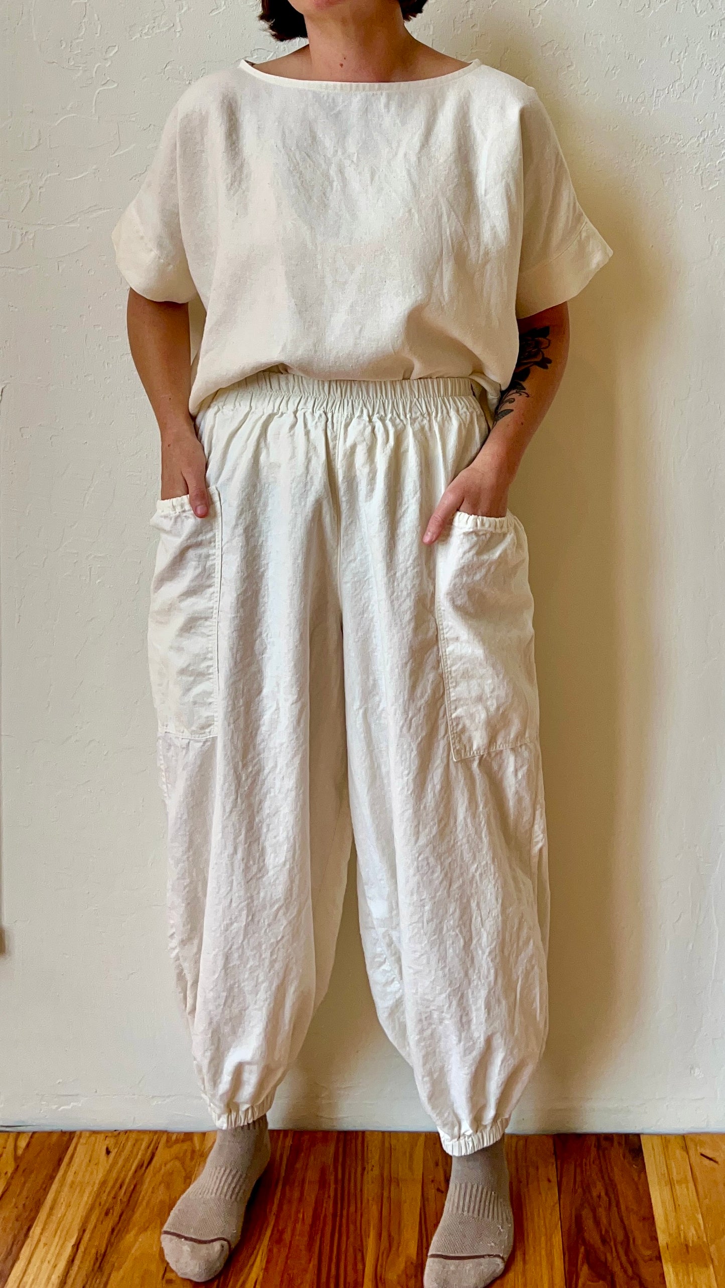 Person wearing a white hemp outfit with loose-fitting pants and a top against a plain wall.