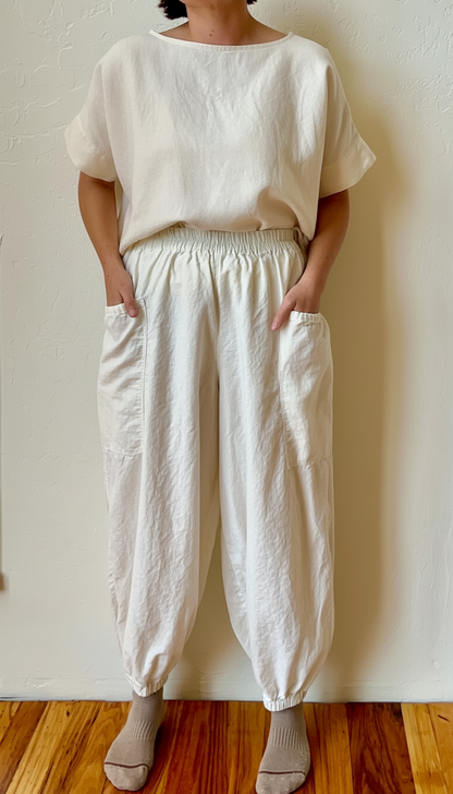 Person wearing a white hemp outfit with loose-fitting pants and a top against a plain wall.