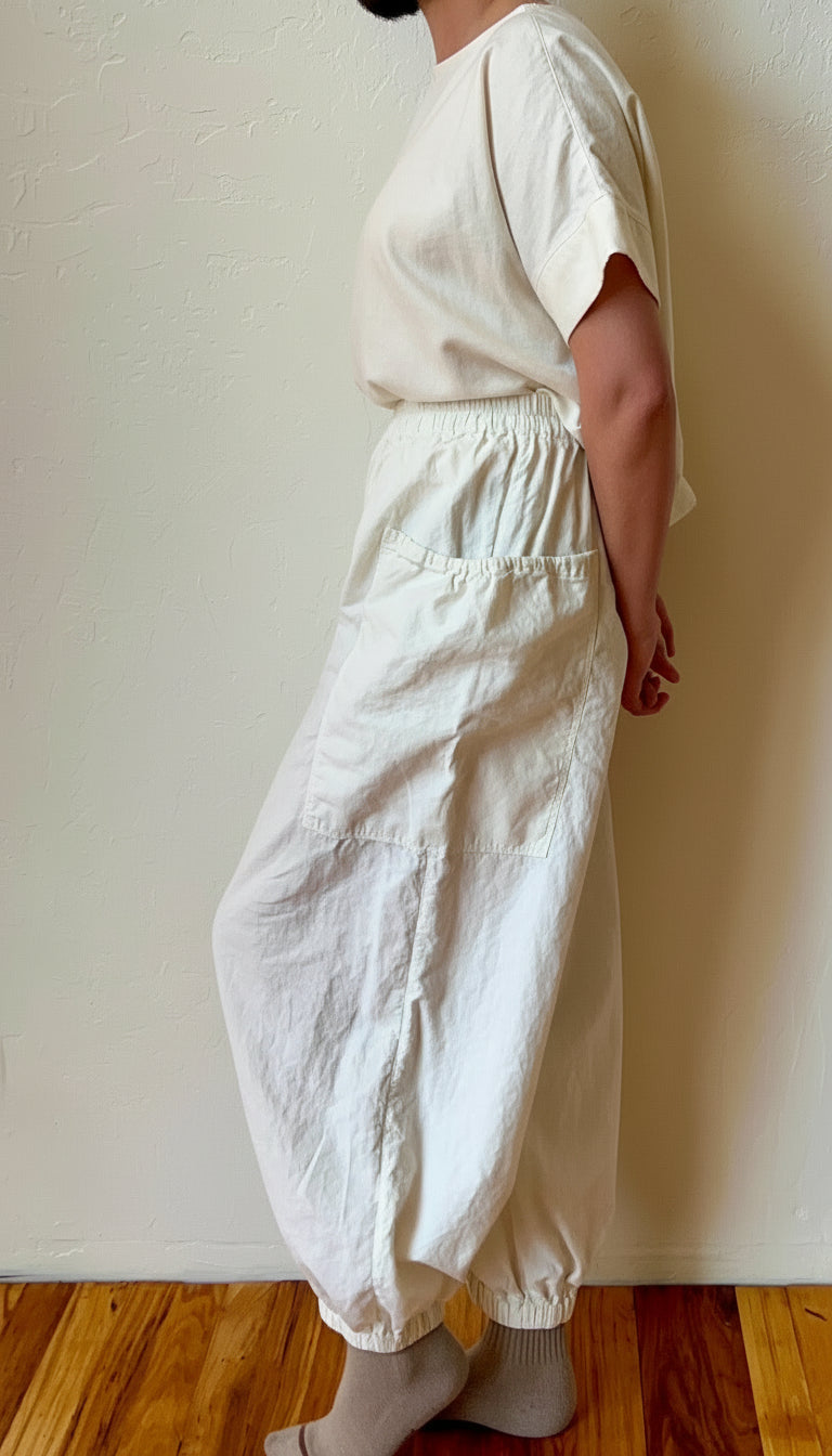 Person wearing a white outfit with wide-leg cargo pants against a plain wall.