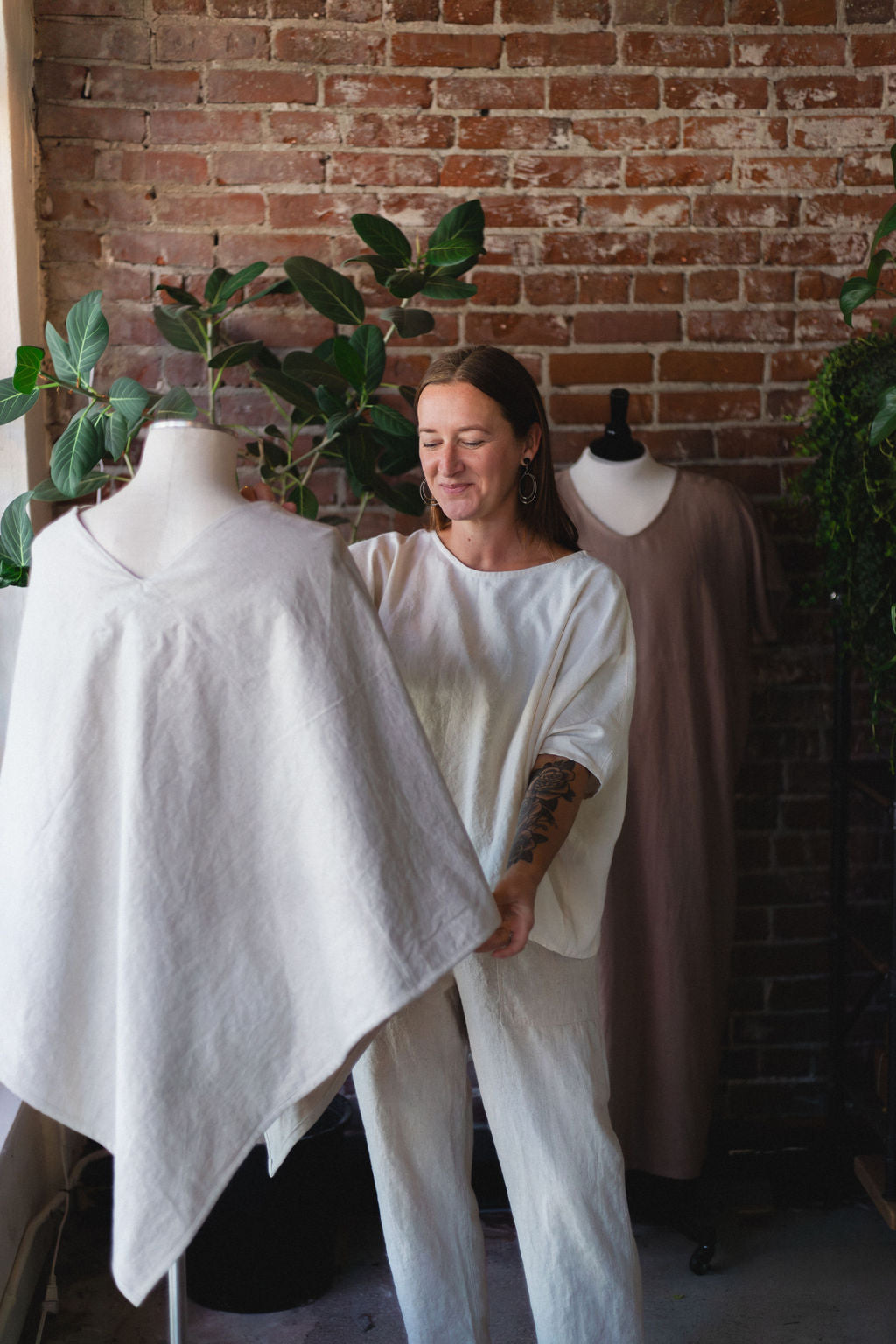 Person holding a hemp poncho jacket on a mannequin against a brick wall.