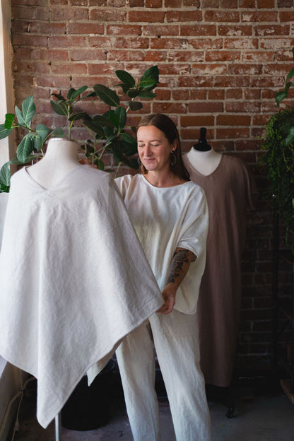 Person holding a hemp poncho jacket on a mannequin against a brick wall.