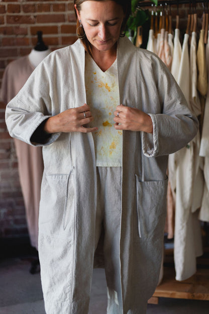 Person wearing a light gray outfit with a patterned shirt in a clothing store.