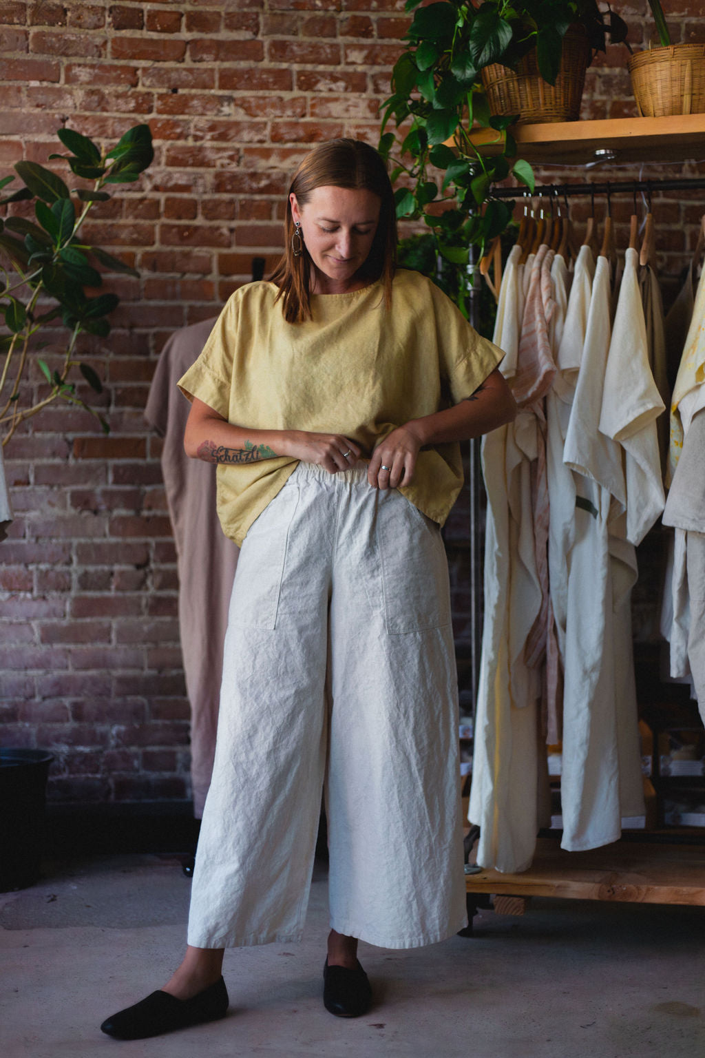 Woman wearing a yellow top and white hemp pants standing in a clothing store.