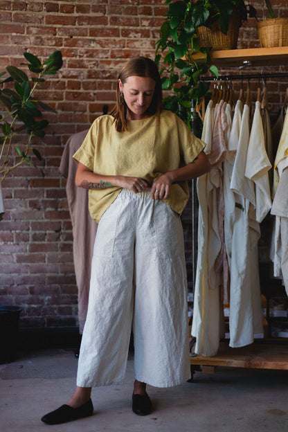 Woman wearing a yellow top and white hemp pants standing in a clothing store.